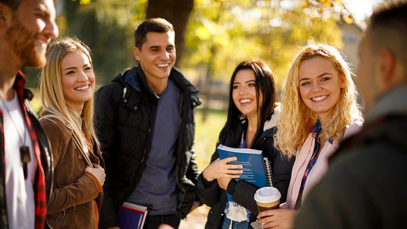 Five student together talking on campus listening to a tour guide