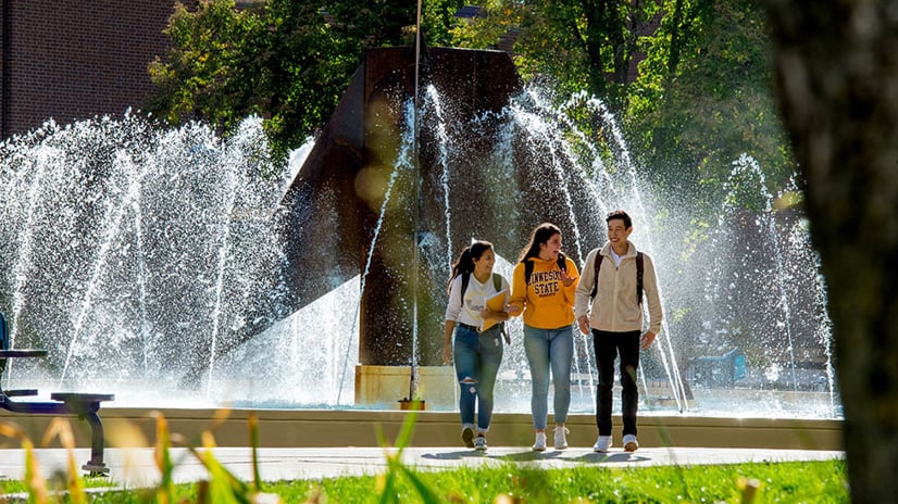 a group of people walking in front of a fountain
