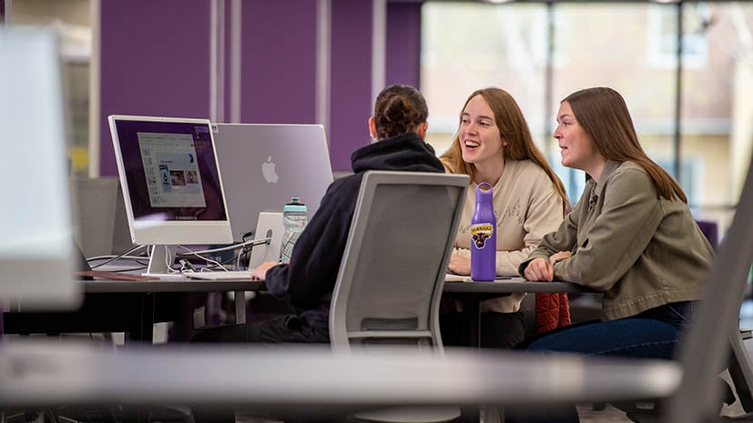 Three individuals meeting together around a table with a computer