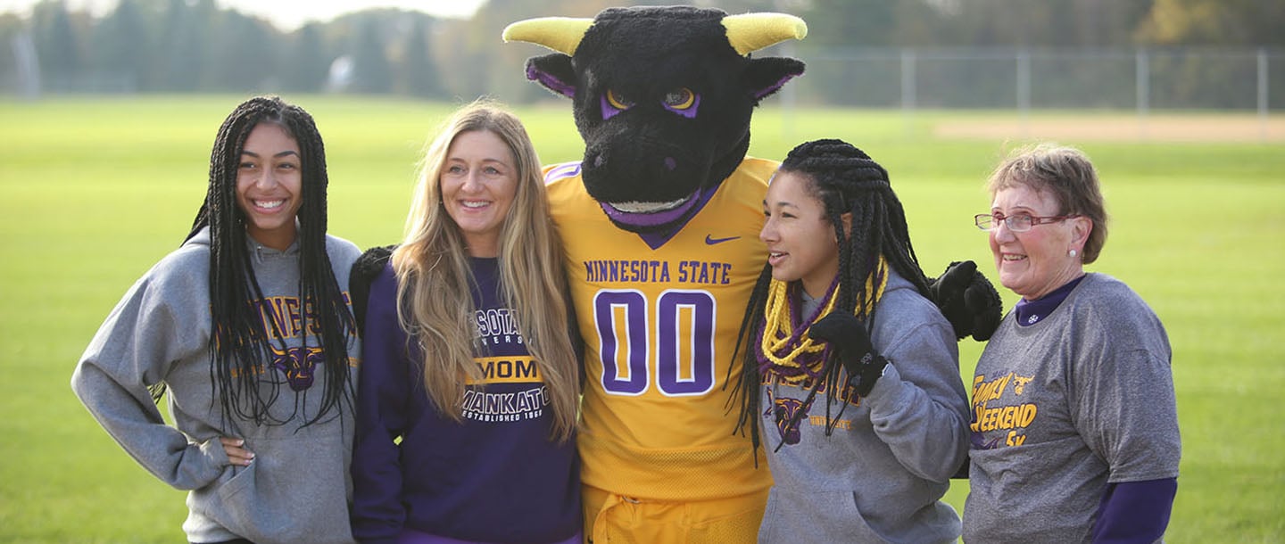 Two mothers, and their daughters, taking picture with the mascot, Stomper.