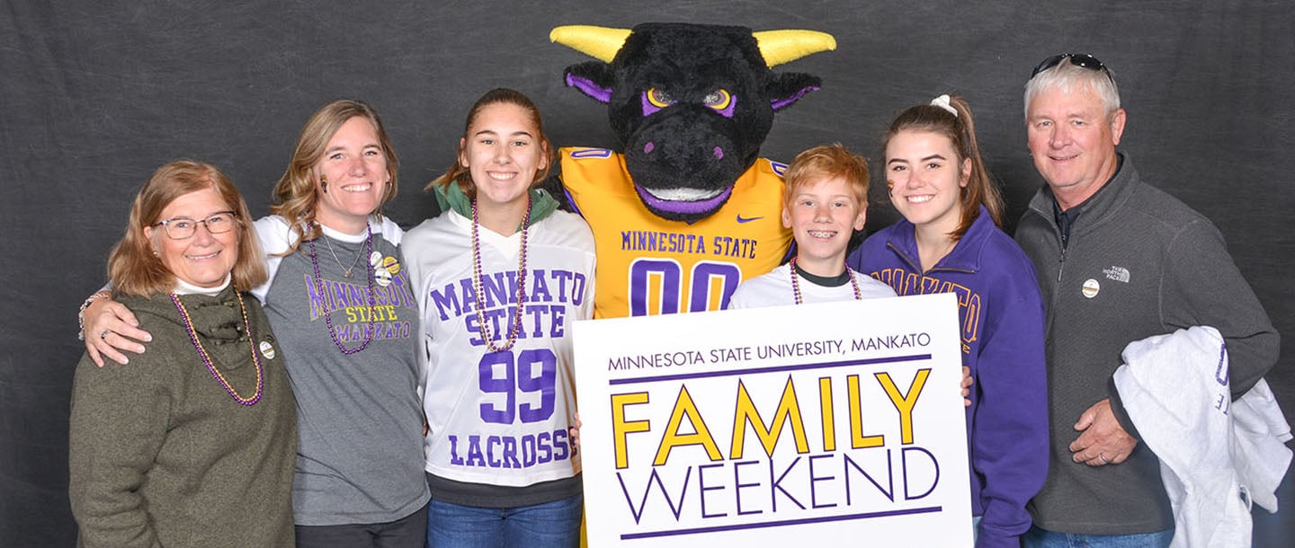 A family posing with the mascot, stomper, during family weekend