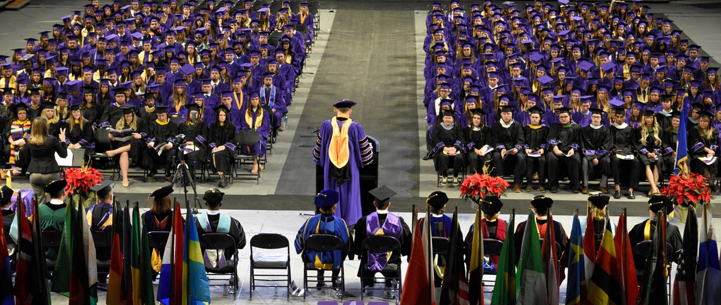 A person wearing purple hat and gown on a stage giving a speech to the new graduates at the commencement ceremony