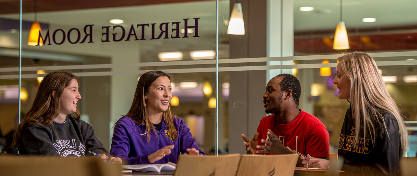 Four students sitting together at a table and having a discussion in the Heritage Room