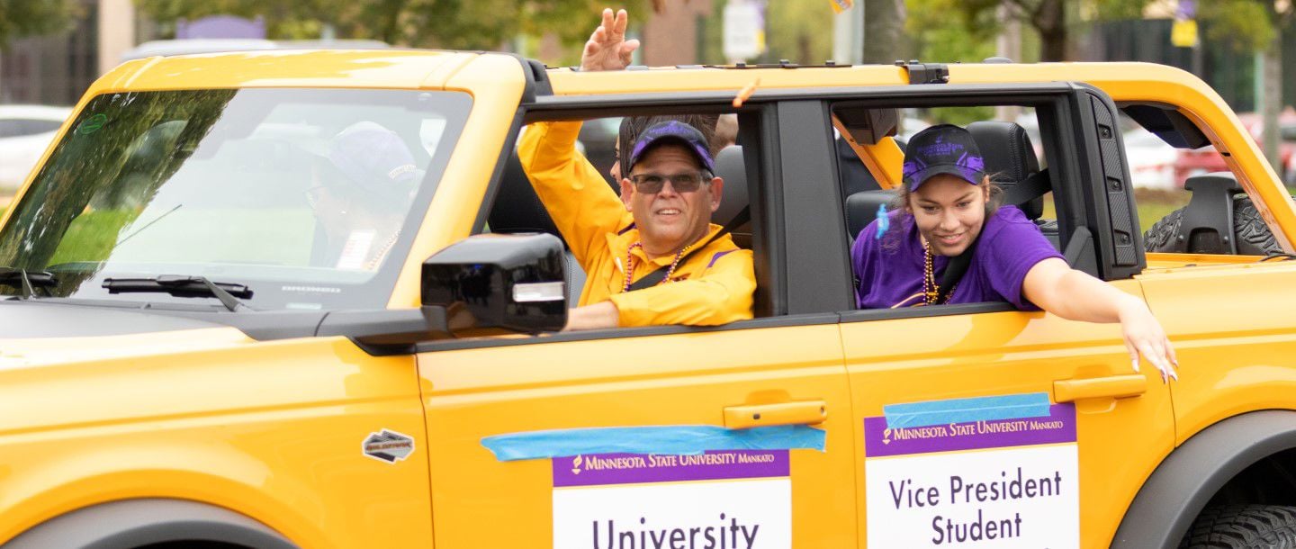 President Inch and multiple students driving together in a yellow car at Homecoming parade