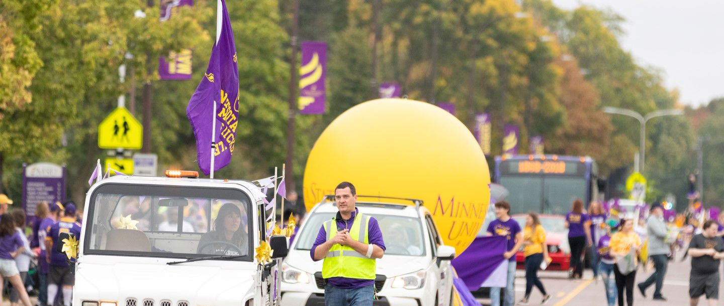 A traffic controller controlling cars with many people walking on the roads and side walks at homecoming parade