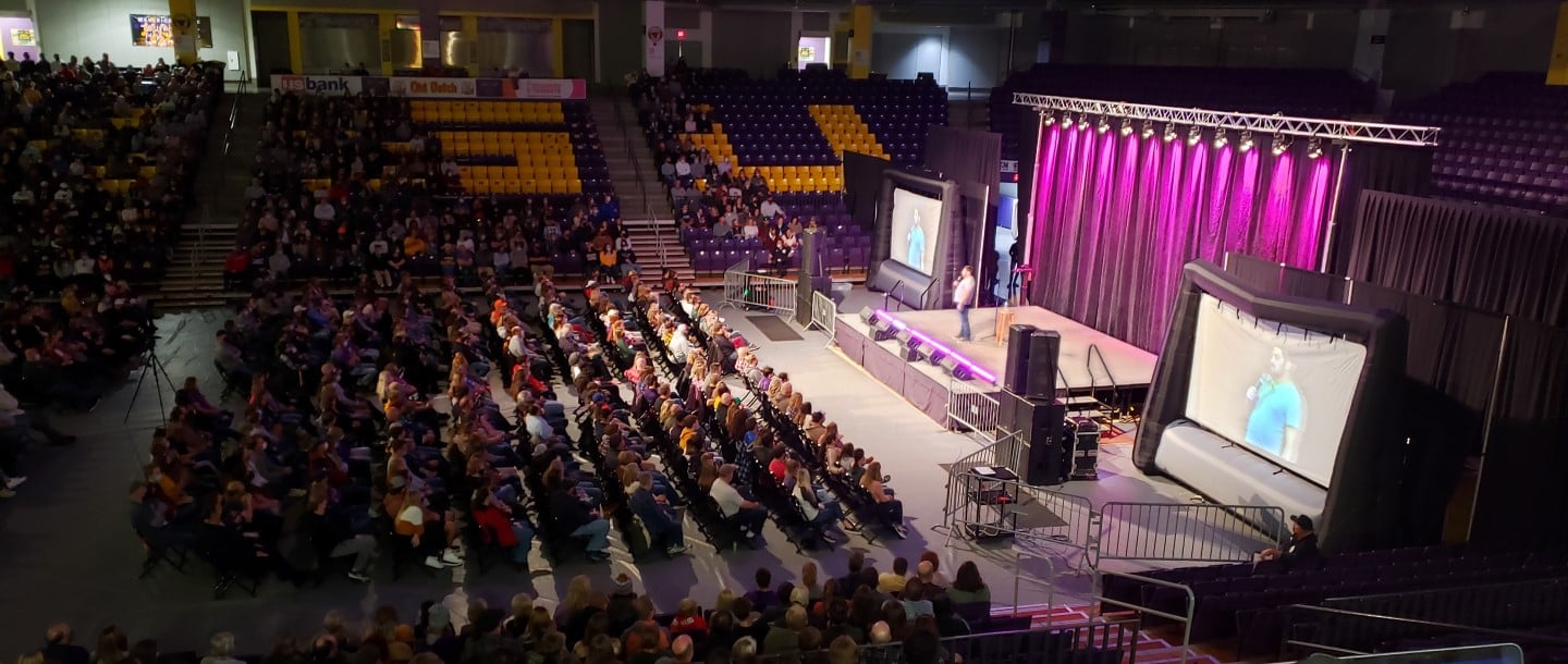 Charlie Berens at Minnesota State University, Mankato Taylor Center on a stage speaking into a mic in front of an audience