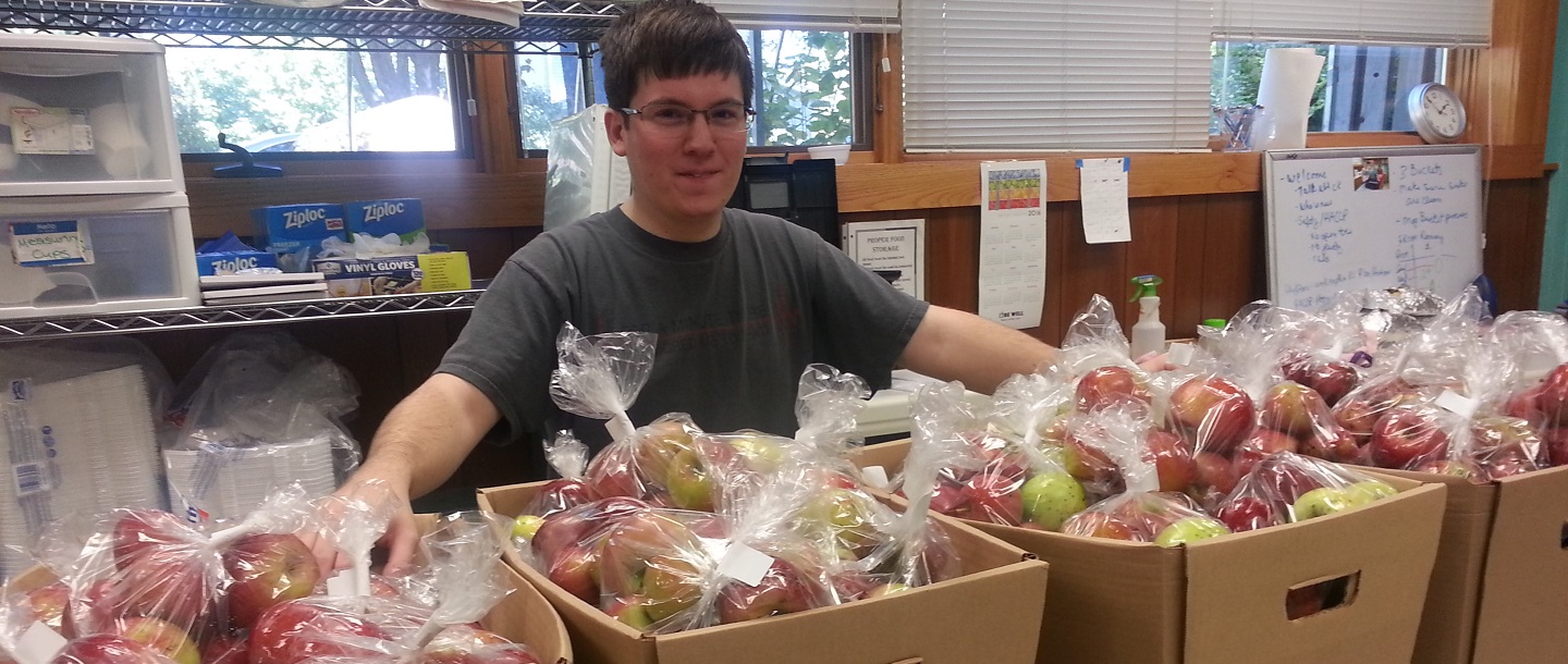 Student stands in front of donated apples that have been bagged by volunteers.