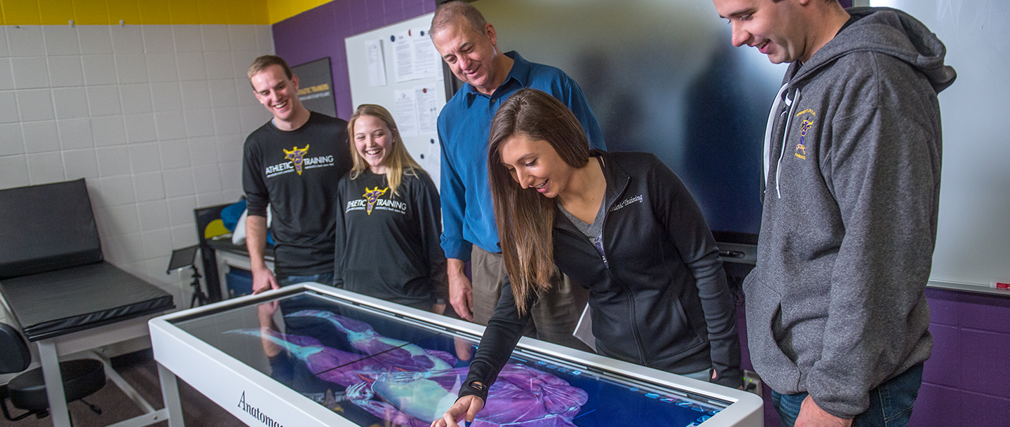 Four athletic training students with their professor around an interactive human anatomy application table