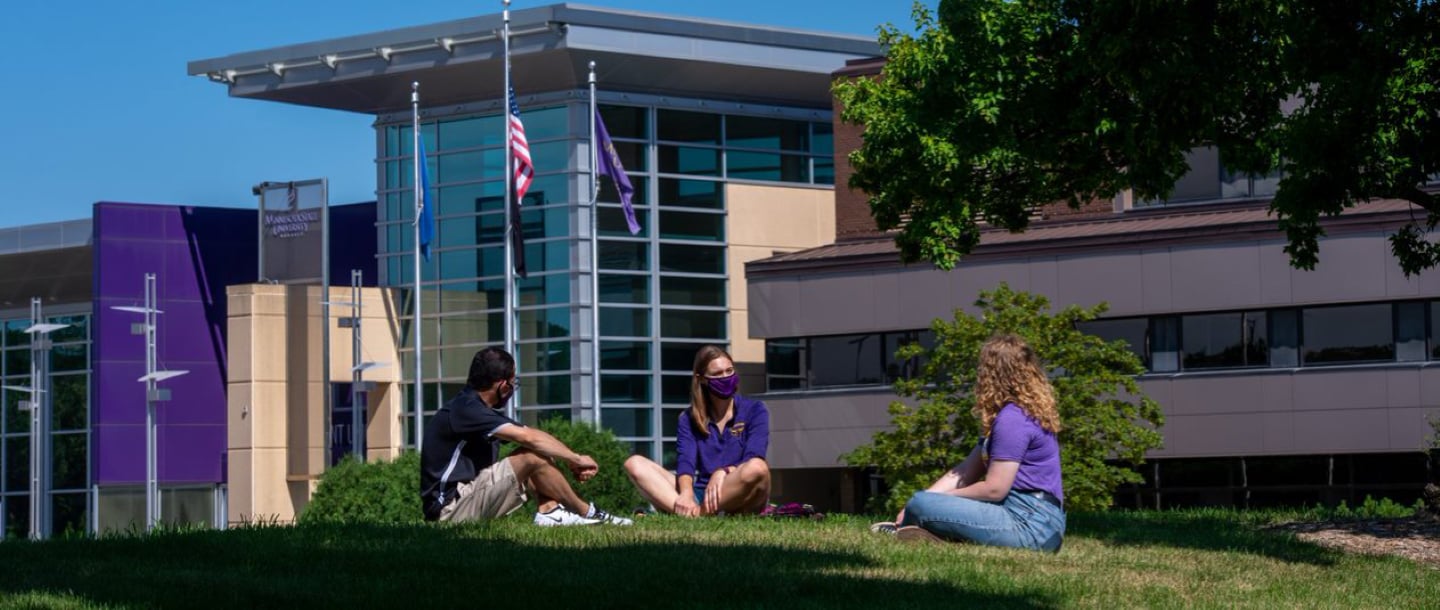 students wearing mask sitting down on the lawn in front of the Centennial Student Union building