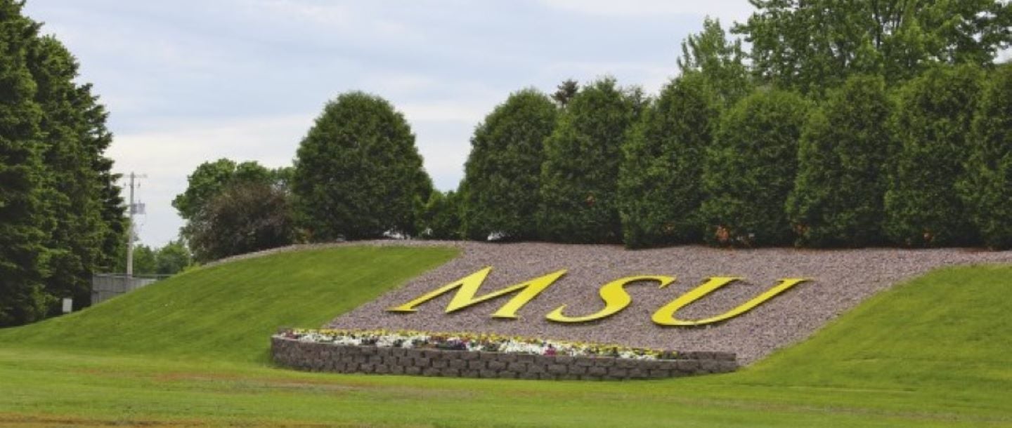 Yellow letters MSU positioned on a small mound in front of the football field