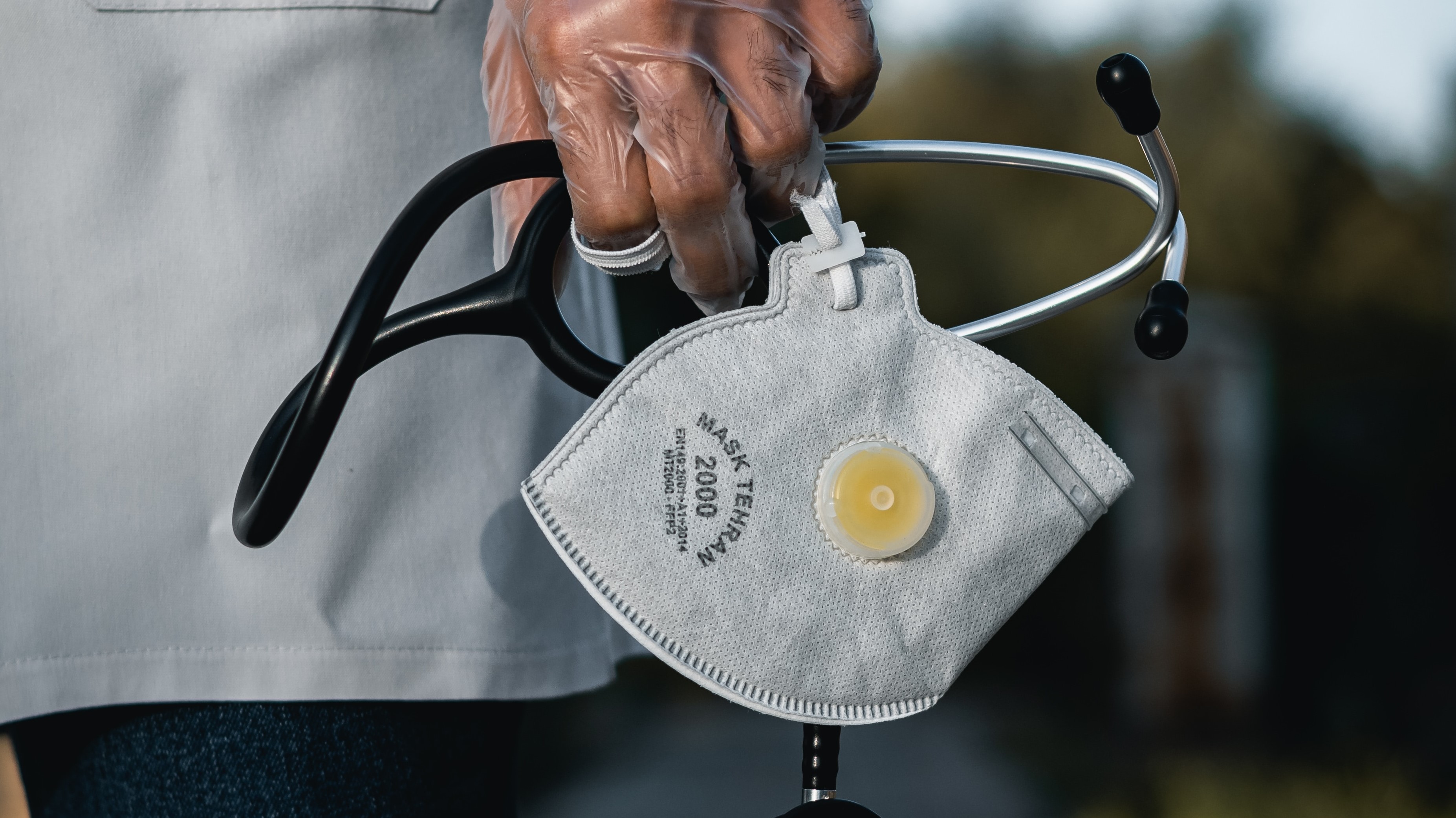 Stock photo of a medical professional in a white coat holding an N-95 mask and a stethoscope.