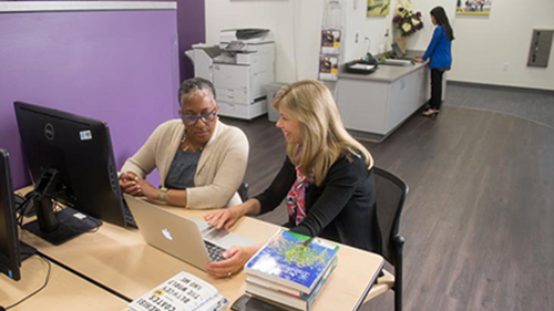 One individual showing another information on a laptop screen