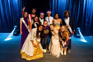 Members of the Homecoming Royalty Court of 2021 posing for a photo on the stage inside campus wearing white sashes