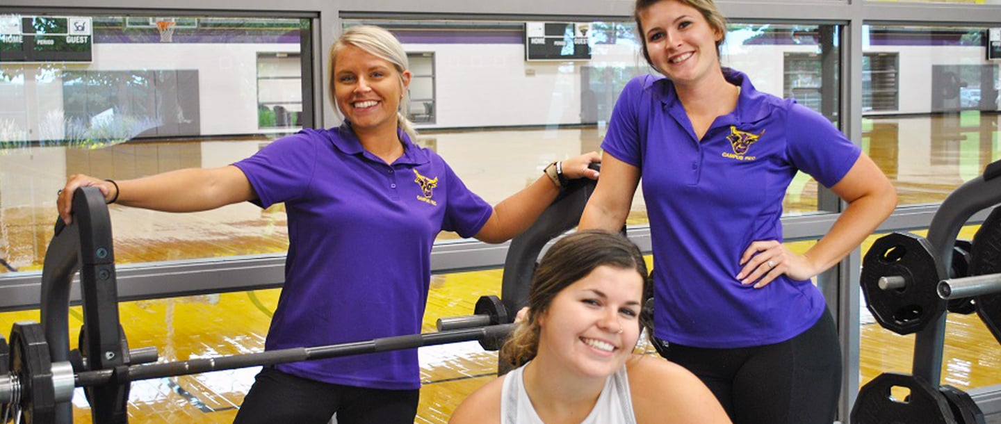 Three female trainers in campus recreation weight room