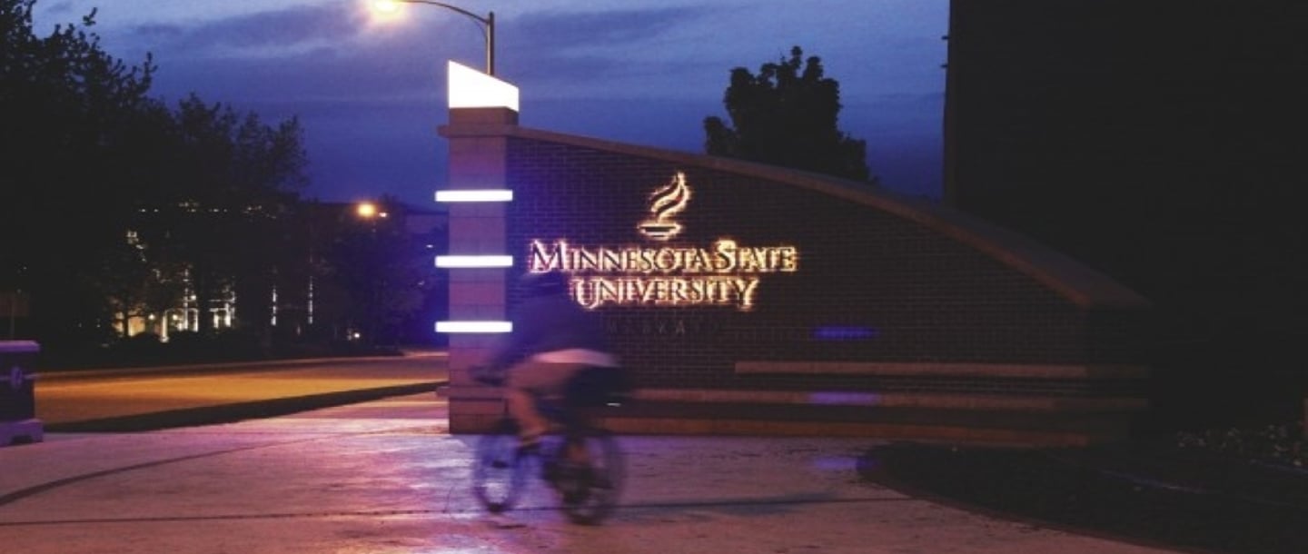1 person cycling inront of the Minnesota State University logo at the entrance