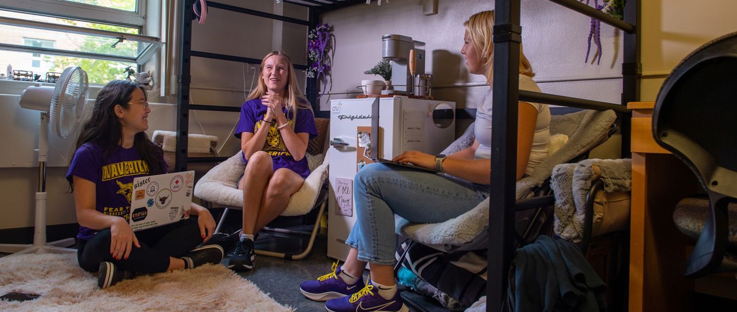 Three students hanging out in their dorm talking and studying together