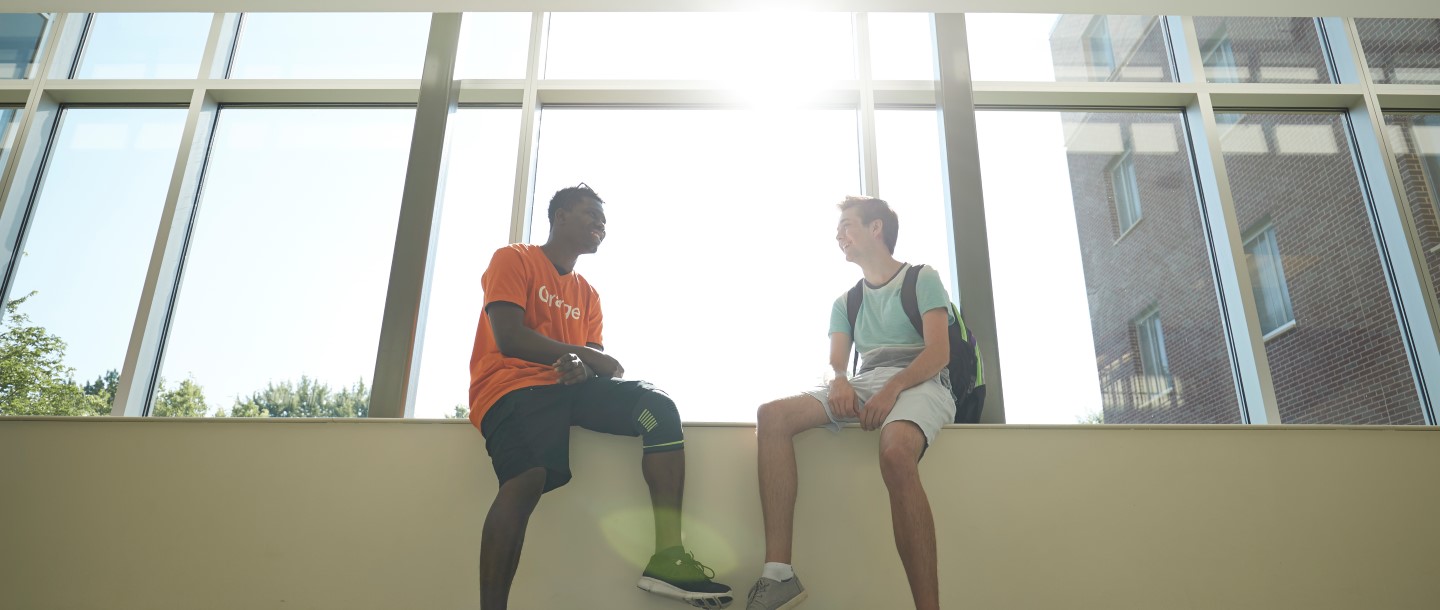 Two guys sitting next to windows in the Julia Sears residence community hallway