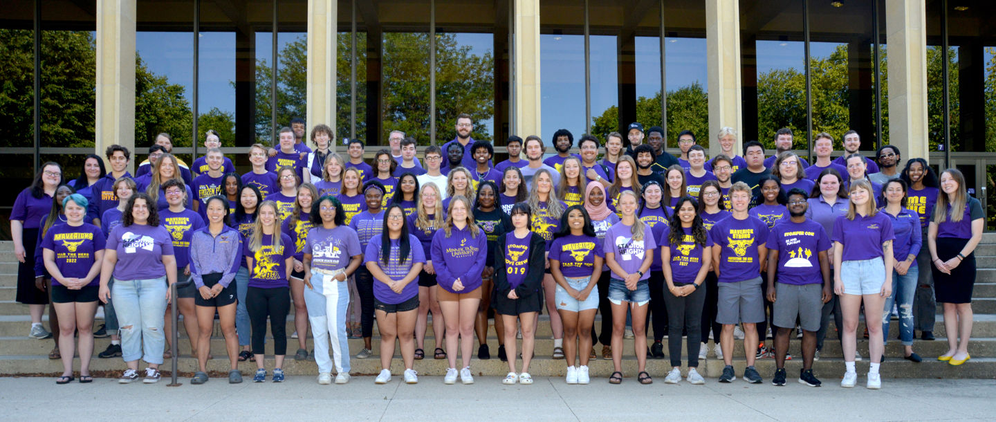 A group of students standing outside on steps posing with Minnesota State University Mankato short sleeve purple T-shirts and smiling
