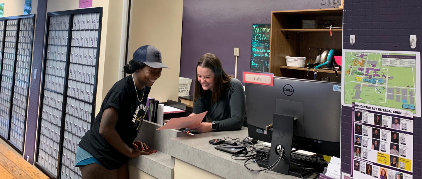 Front desk assistant laughing with a student while holding a form and looking at it together