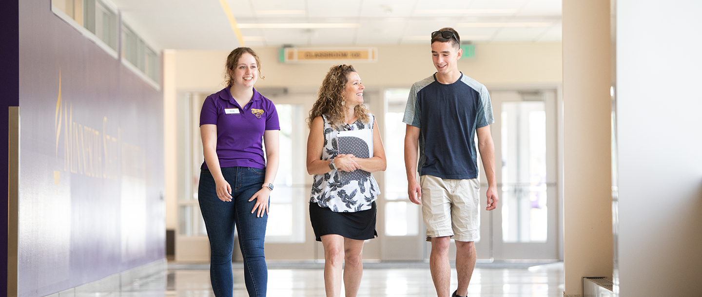 A student campus tour guide walking with a parent and student in the hallway on campus