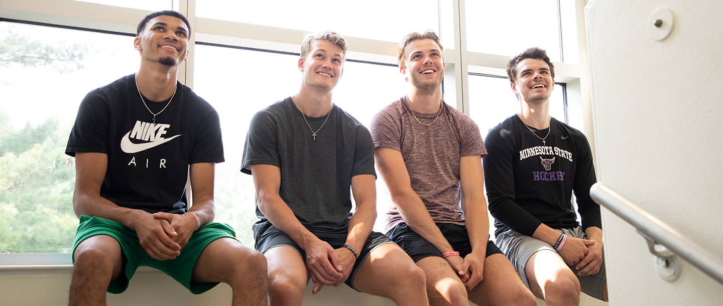 Four students sitting together inside campus next to windows