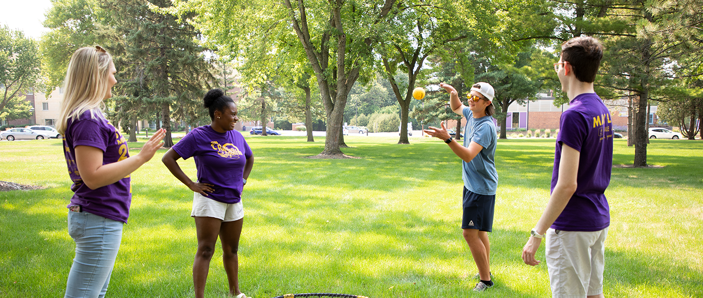 Four students outside in a circle playing with a small yellow ball