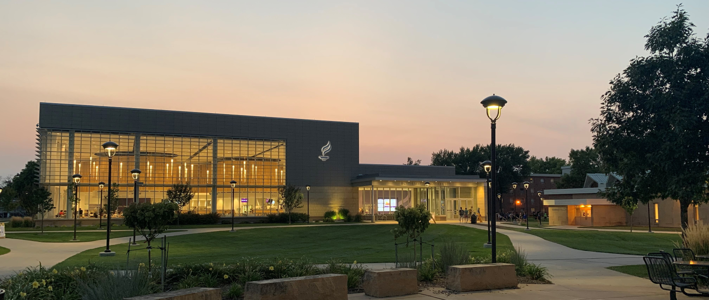 View of the University dinning center building at dusk with students eating inside and students walking around outside