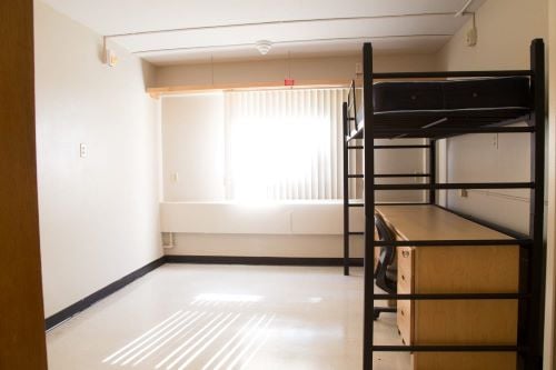 View of an empty basic single room with bed and desk