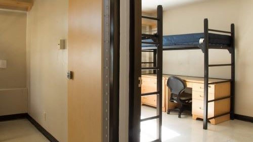 View of a basic full-bath suite with beds and desk for three students