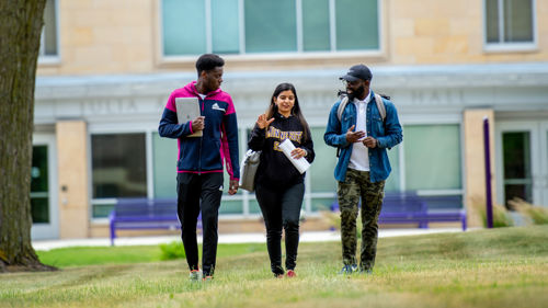 Three students talking and walking on the lawn outside of Julia Sears