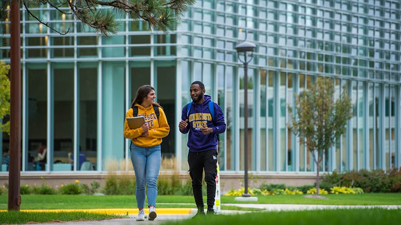 two students walking on campus with a large campus building in the background