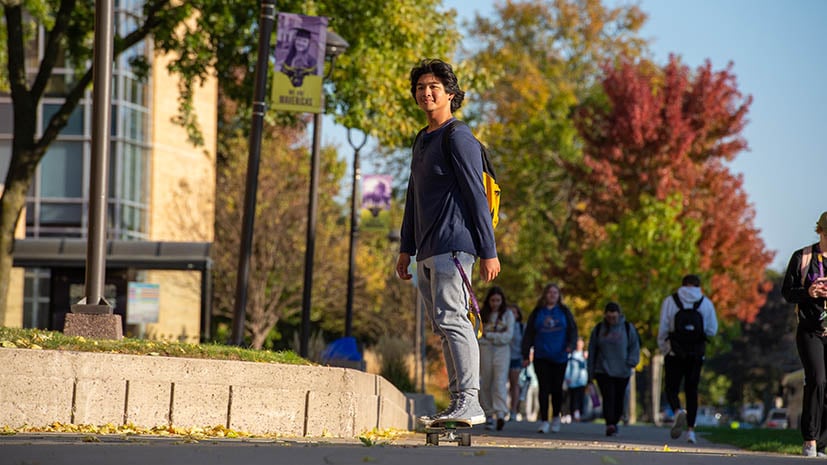 student on skateboard on campus with autumn colors in the background