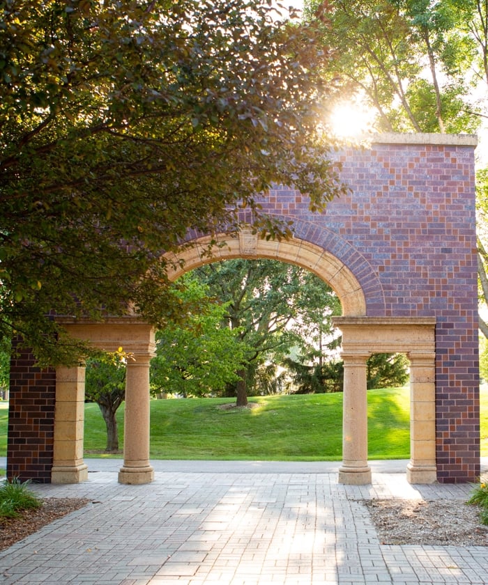View of campus through the arch showcasing the trees, greenery, and academic buildings