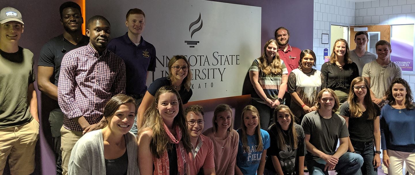group of students posing in front of a wall with the Minnesota State University, Mankato logo